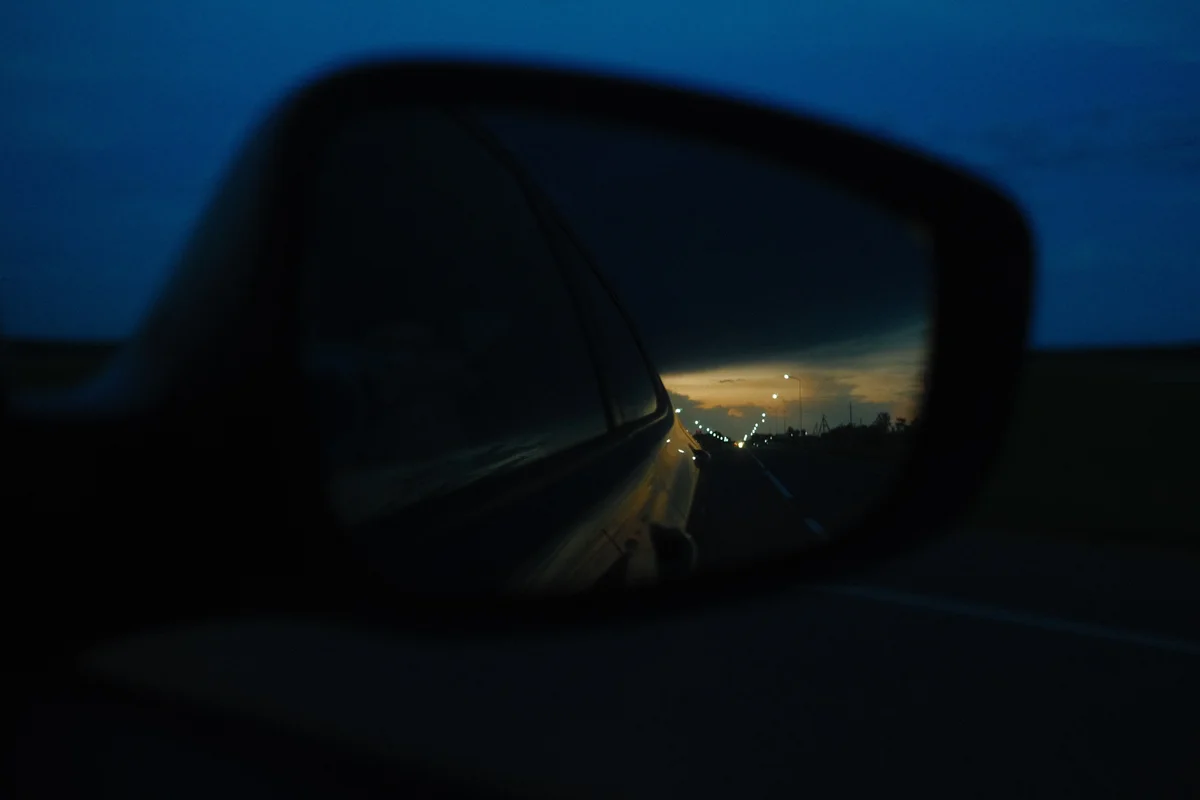 Dusk and distant lights reflected in a car mirror.