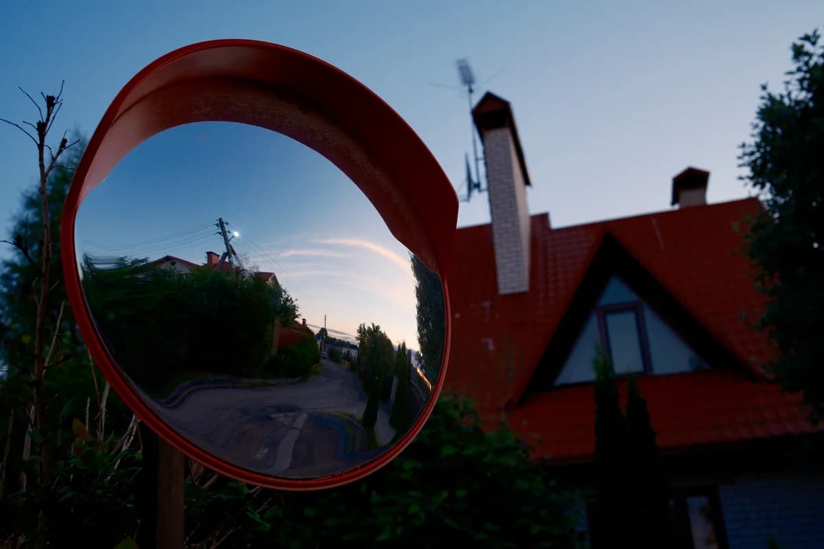 An evening street reflected in a red roadside mirror.